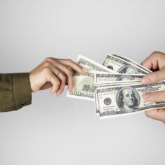 Uma mão segura muitas notas de dinheiro, enquanto outra tenta puxar apenas uma, representando monopólio de categoria