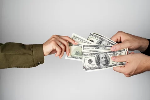 Uma mão segura muitas notas de dinheiro, enquanto outra tenta puxar apenas uma, representando monopólio de categoria