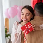 Casal abraçado com moça segurando um presente em uma das mãos