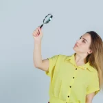 Mulher de camisa amarela usando uma lupa para encontrar produtos para vender em fundo branco