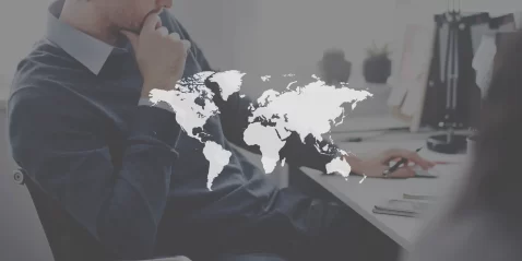 Executivo ao fundo com um mapa mundi a sua frente em preto e branco