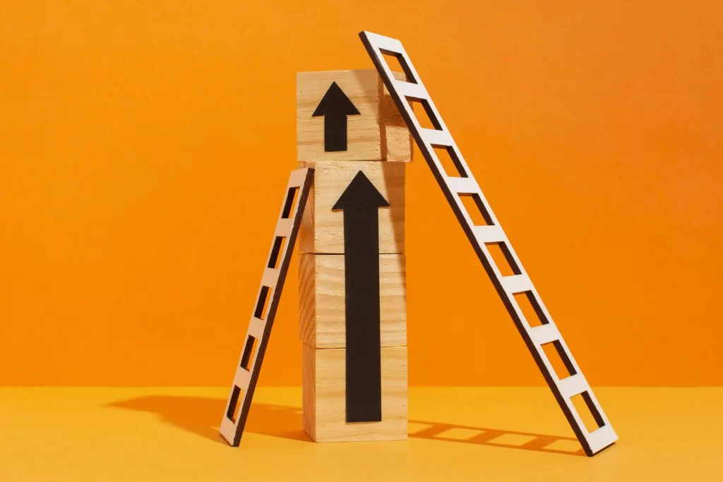 Blocos formando duas setas pretas apontando para cima apoiadas por uma escada de cada lado em fundo amarelo
