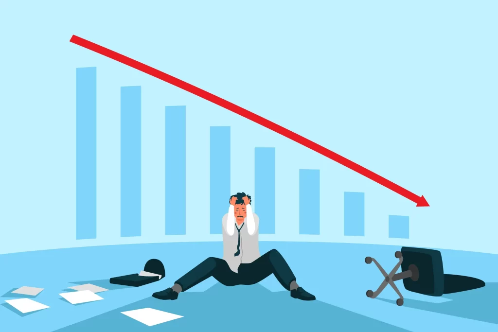 Homem sentado no chão com as mãos na cabeça com um gráfico de queda acentuada ao fundo