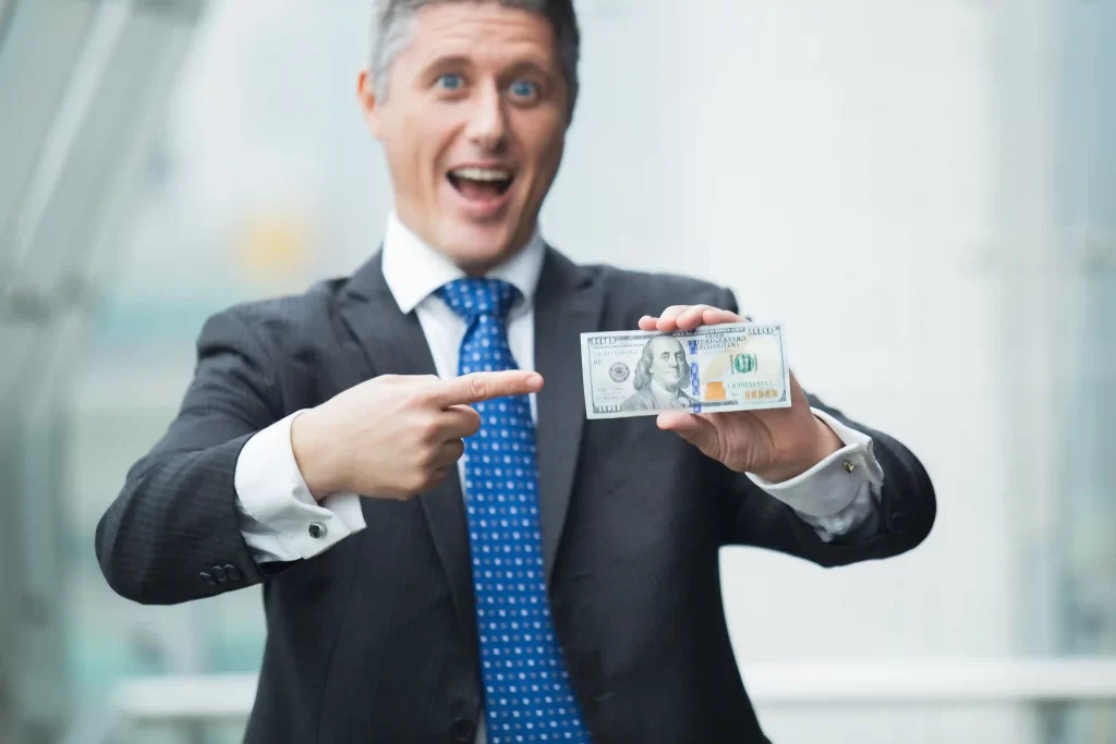 Homem americano de terno segurando dólares e apontando para eles