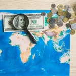 Mapa do mundo com notas e moedas de dólares sob uma lupa