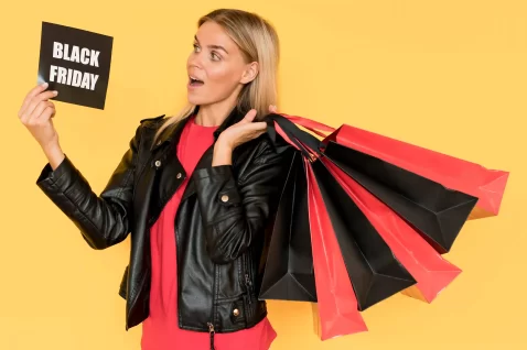 Mulher om várias bolsas de compras vermelhas e pretas com uma placa de Balck Friday em fundo amarelo