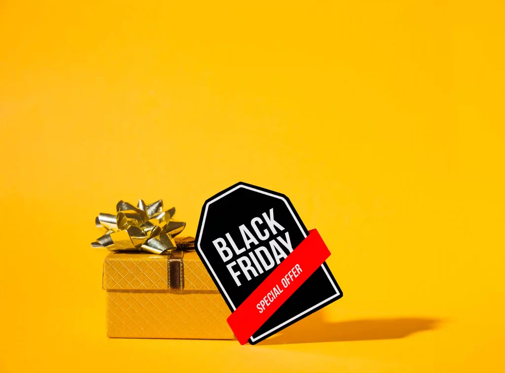 Embalagem de presente amarela com laço dourado ao lado de uma tag preta da Black Friday em fundo amarelo