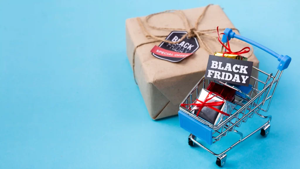 Carrinho de compras com presentes e uma plaquinha escrito Black Friday com um pacote ao fundo