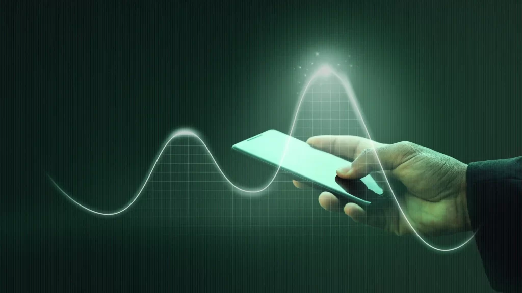 Homem segurando celular perto de um gráfico preto com linha verde que mostra uma onda de vendas