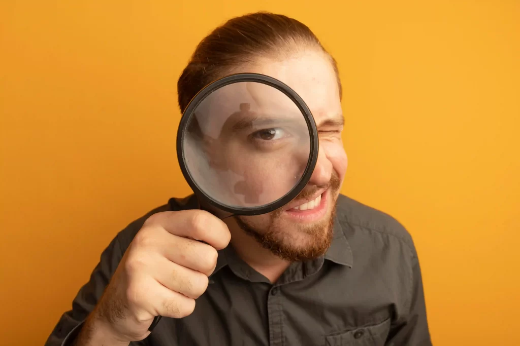 Homem com lupa em frente ao rosto em fundo amarelo