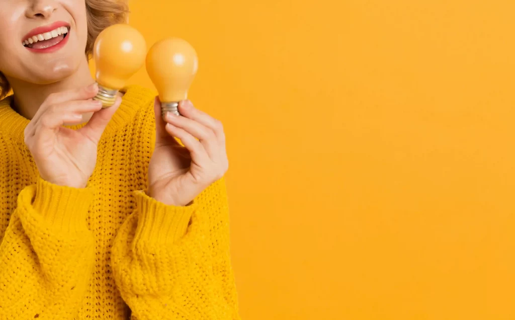 Vendedora de casaco amarelo segurando lâmpadas amarelas em fundo amarelo