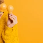 Vendedora de casaco amarelo segurando lâmpadas amarelas em fundo amarelo