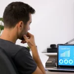 Homem com a mão no queixo analisando dados em seu notebook em escritório