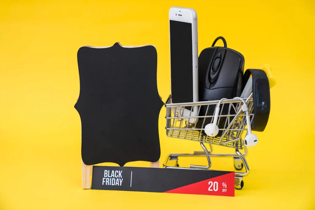 Carrinho de compras com três itens ao lado de um quadro negro e uma placa escrito Black Friday em fundo amarelo