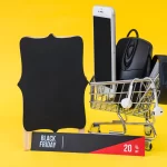 Carrinho de compras com três itens ao lado de um quadro negro e uma placa escrito Black Friday em fundo amarelo