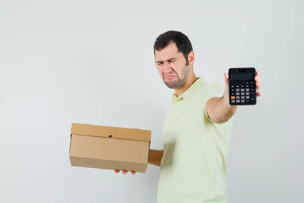 Homem segurando uma caixa com uma mão e uma calculadora na outra