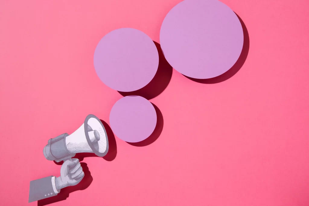 Mão segurando megafone com círculos lilás em frente em fundo rosa