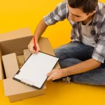 Jovem sentado no chão ao lado de caixas de papelão abertas, preenchendo uma prancheta, simbolizando os primeiros 90 dias vendendo no Mercado Livre