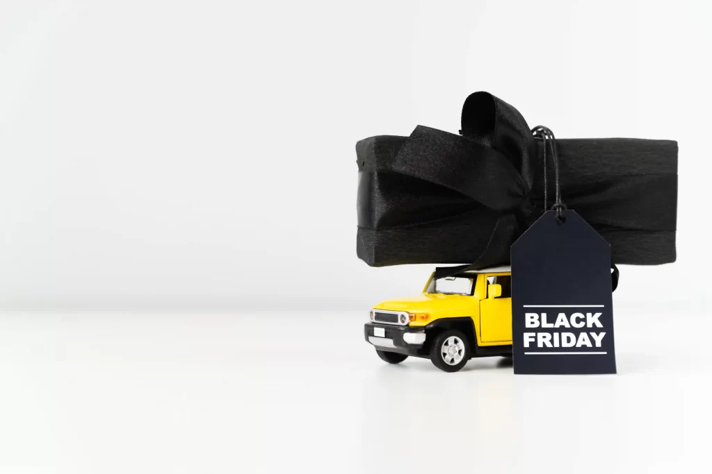 Miniatura de caminhão amarelo transportando presente embrulhado em preto com etiqueta Black Friday.