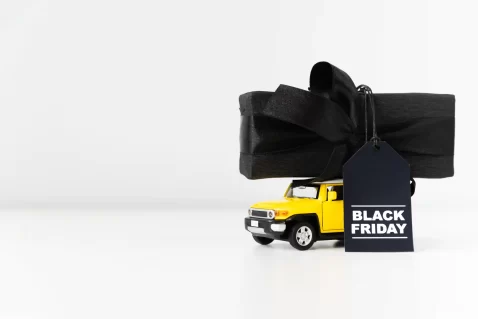 Miniatura de caminhão amarelo transportando presente embrulhado em preto com etiqueta Black Friday.