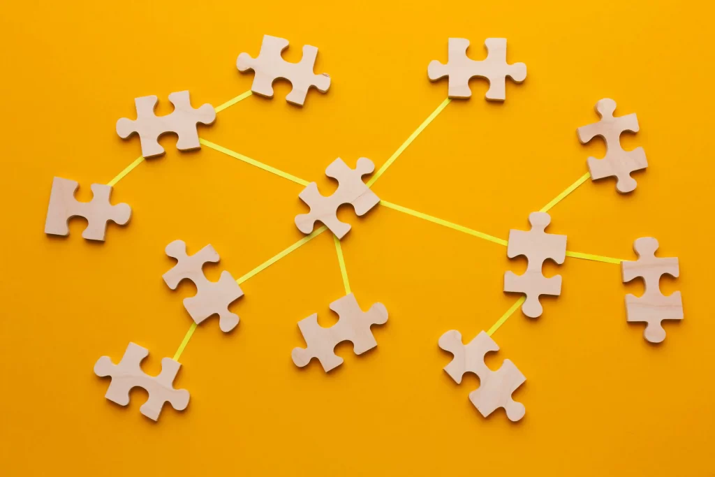 Várias peças de quebra-cabeças cinzas interligadas por um barbante amarelo em fundo laranja