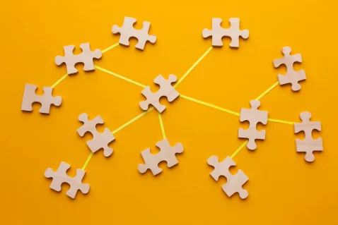 Várias peças de quebra-cabeças cinzas interligadas por um barbante amarelo em fundo laranja