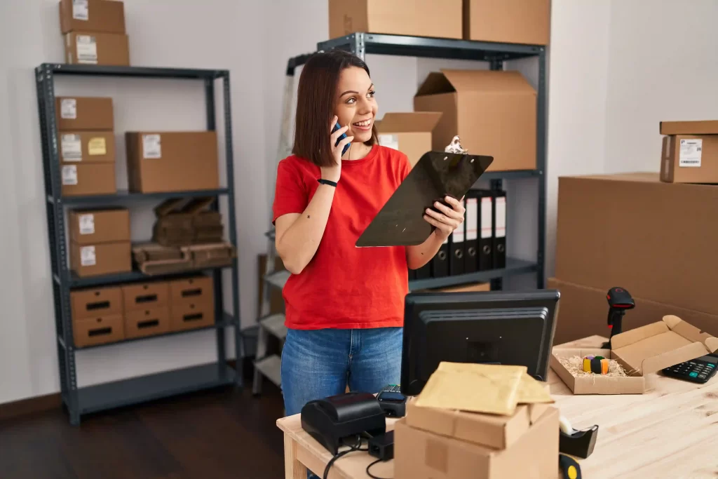 Empreendedora em depósito organizando pedidos com prancheta, caixas e estoque de e-commerce.