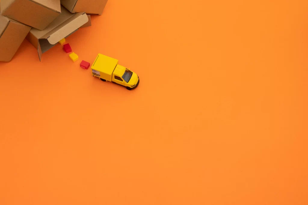 Caixas de entrega na canto alto com um caminhão amarelo do Mercado Livre saindo de perto em fundo laranja