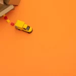 Caixas de entrega na canto alto com um caminhão amarelo do Mercado Livre saindo de perto em fundo laranja