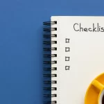 Caderno de checklist aberto sobre fundo azul com xícaras de café, representando planejamento para checklist Mercado Livre