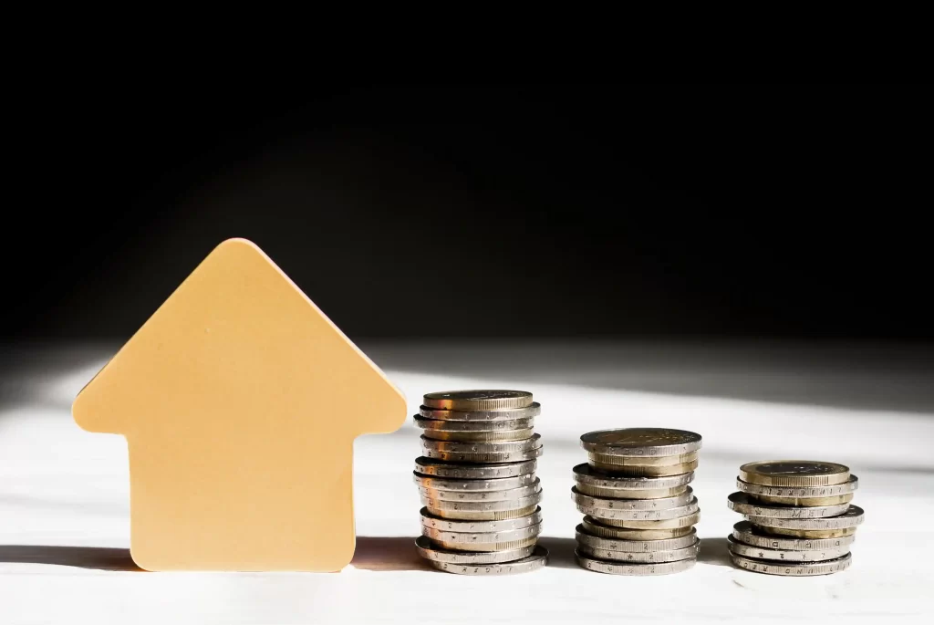 Ícone de casa ao lado de pilhas de moedas empilhadas em diferentes alturas, representando crescimento financeiro e análise de micro-nichos rentáveis