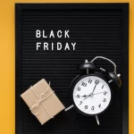 Relógio despertador preto e presente sobre quadro com as palavras Black Friday, representando o senso de urgência e o uso de dados em tempo real para aproveitar o pico de vendas