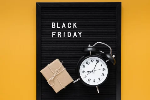 Relógio despertador preto e presente sobre quadro com as palavras Black Friday, representando o senso de urgência e o uso de dados em tempo real para aproveitar o pico de vendas