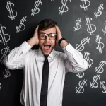 Homem de camisa branca e gravata preta, com expressão surpresa e mãos na cabeça, em frente a um quadro cheio de símbolos de cifrão desenhados, representando confusão com gargalos de lucro