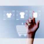 Mão tocando uma tela digital transparente com ícones de camisetas e um carrinho de compras, representando a leitura do mercado por meio da tela de categorias da JoomPulse