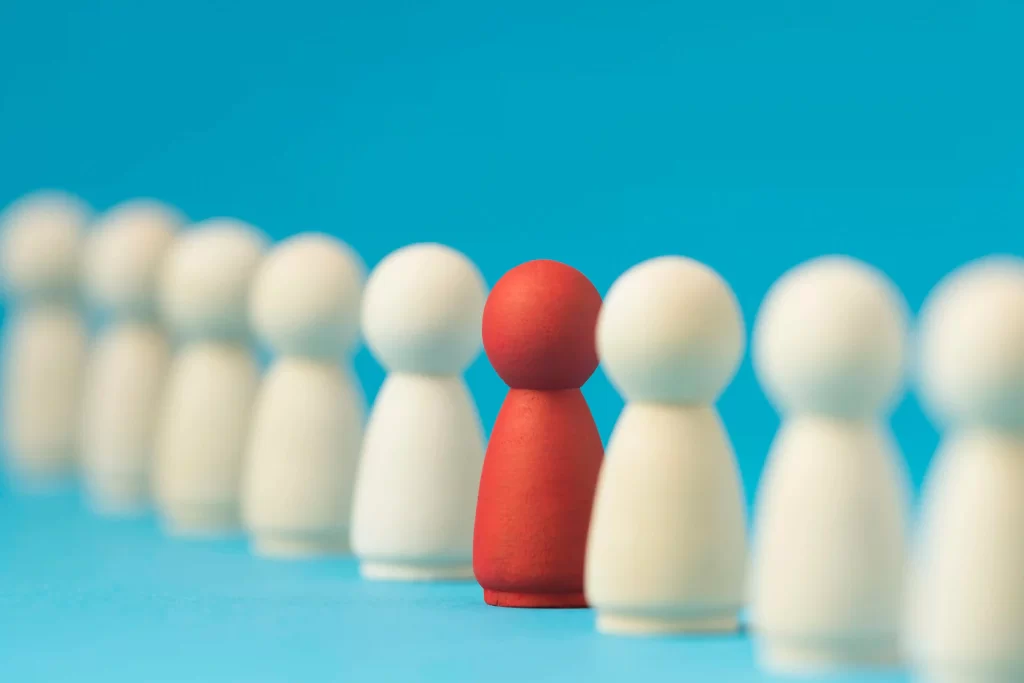 Peças de madeira alinhadas com uma figura vermelha destacada entre figuras brancas, representando diferenciação e identificação de concorrentes indiretos