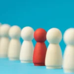 Peças de madeira alinhadas com uma figura vermelha destacada entre figuras brancas, representando diferenciação e identificação de concorrentes indiretos