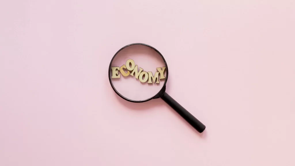 Lupa em fundo rosa ampliando a palavra ‘economy’, simbolizando a observação e análise de mudanças econômicas e inversões de tendência