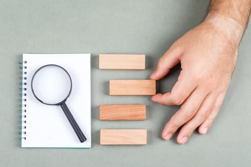 Caderno com lupa e blocos de madeira sendo organizados por uma mão, simbolizando análise e estruturação de dados para identificar um nicho de mercado