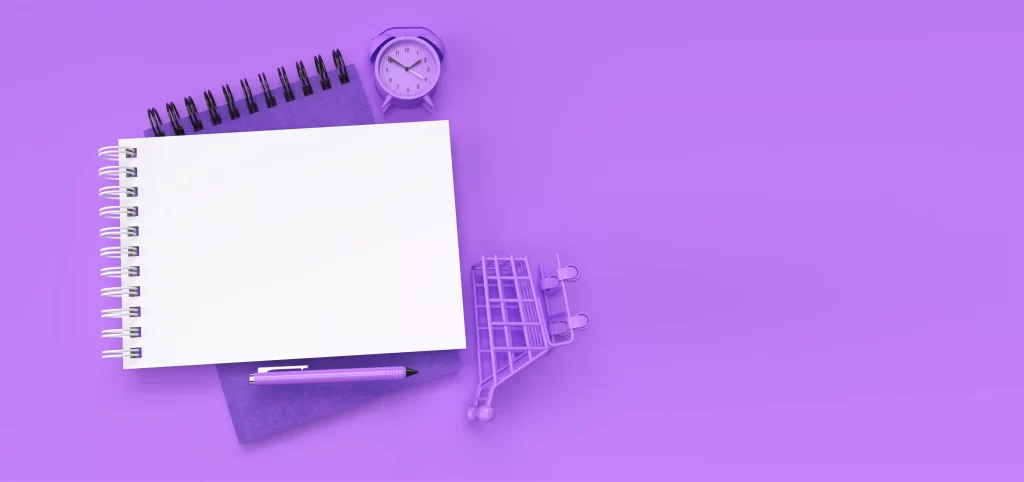 Caderno em branco sobre fundo lilás com caneta, relógio e mini carrinho de compras, simbolizando estratégias de e-commerce para 2026