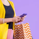 Pessoa segurando o celular e várias sacolas coloridas, simbolizando compras impulsionadas pelo social commerce e integração entre redes sociais e e-commerce