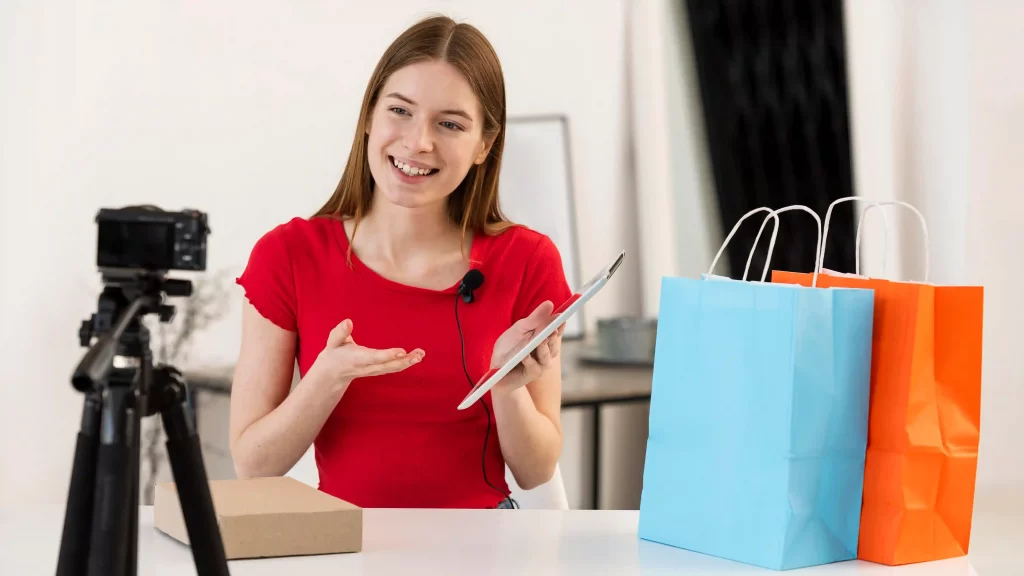 Mulher apresentando produtos e falando diante de uma câmera e sacolas de compras, simbolizando o uso do YouTube Shopping para integrar vídeos e e-commerce
