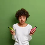 Mulher segurando duas garrafas de bebida, avaliando opções de compra