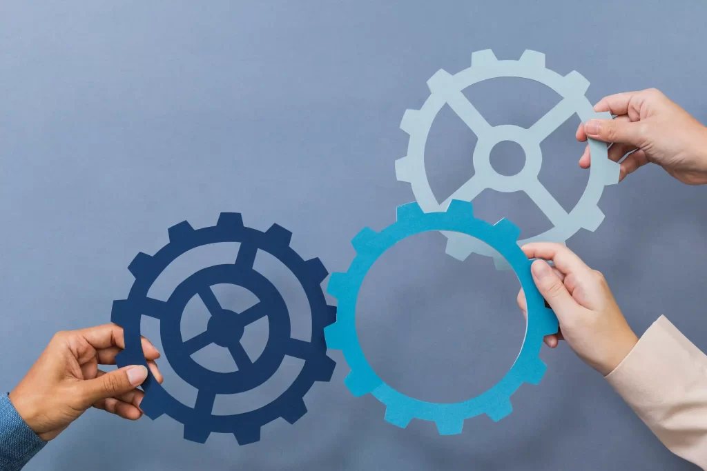 Três mãos segurando engrenagens de papel interligadas, simbolizando ajustes finais