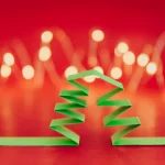 Árvore de Natal estilizada feita de tiras dobradas de papel verde, com luzes desfocadas ao fundo sobre um cenário vermelho
