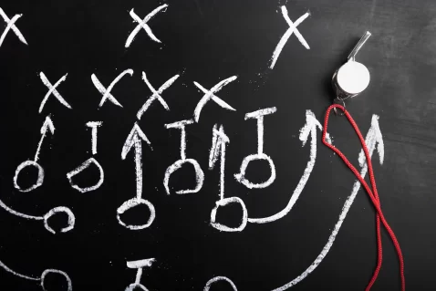 Quadro negro com desenhos de tática em giz e apito pendurado, representando o planejamento para prever reações da concorrência