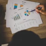 Pessoa analisando relatórios impressos com gráficos e indicadores financeiros.