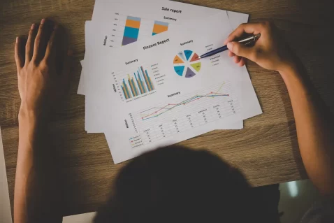 Pessoa analisando relatórios impressos com gráficos e indicadores financeiros.