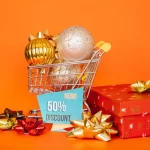 Carrinho de compras com bolas de Natal douradas e prateadas, ao lado de caixa de presente vermelha e placa de desconto de 50%, simbolizando as promoções e os campeões de venda do Natal 2025