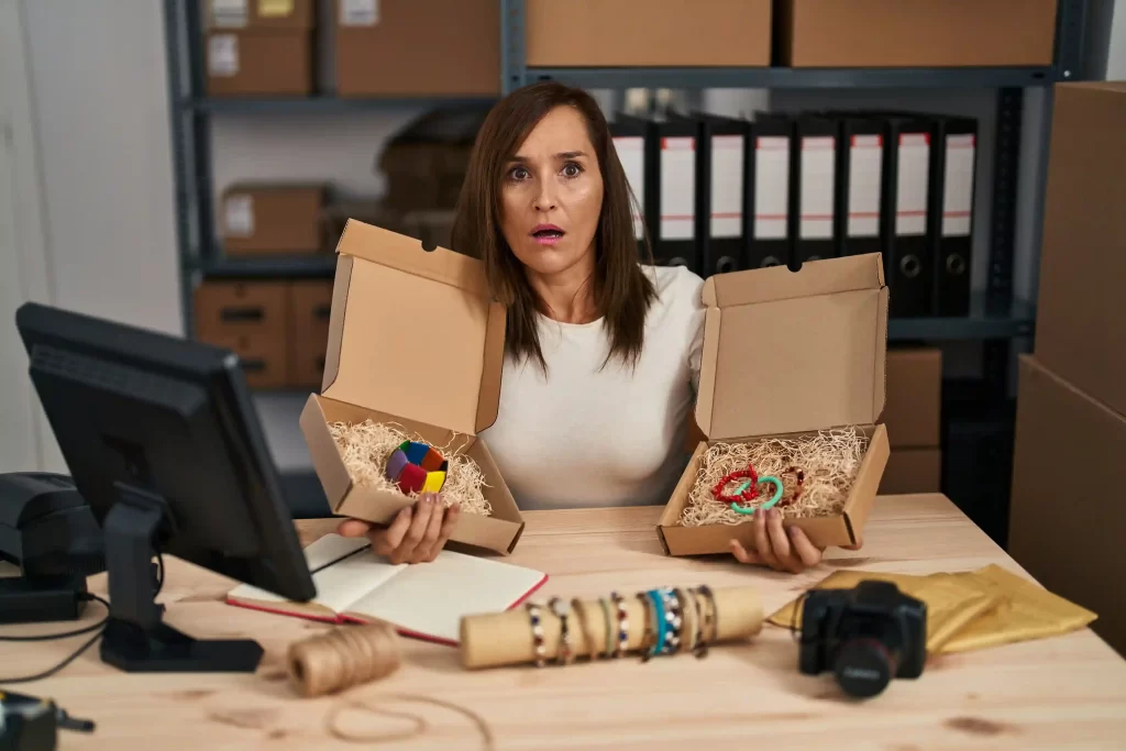 Mulher surpresa segurando duas caixas abertas com produtos artesanais em um ambiente de estoque